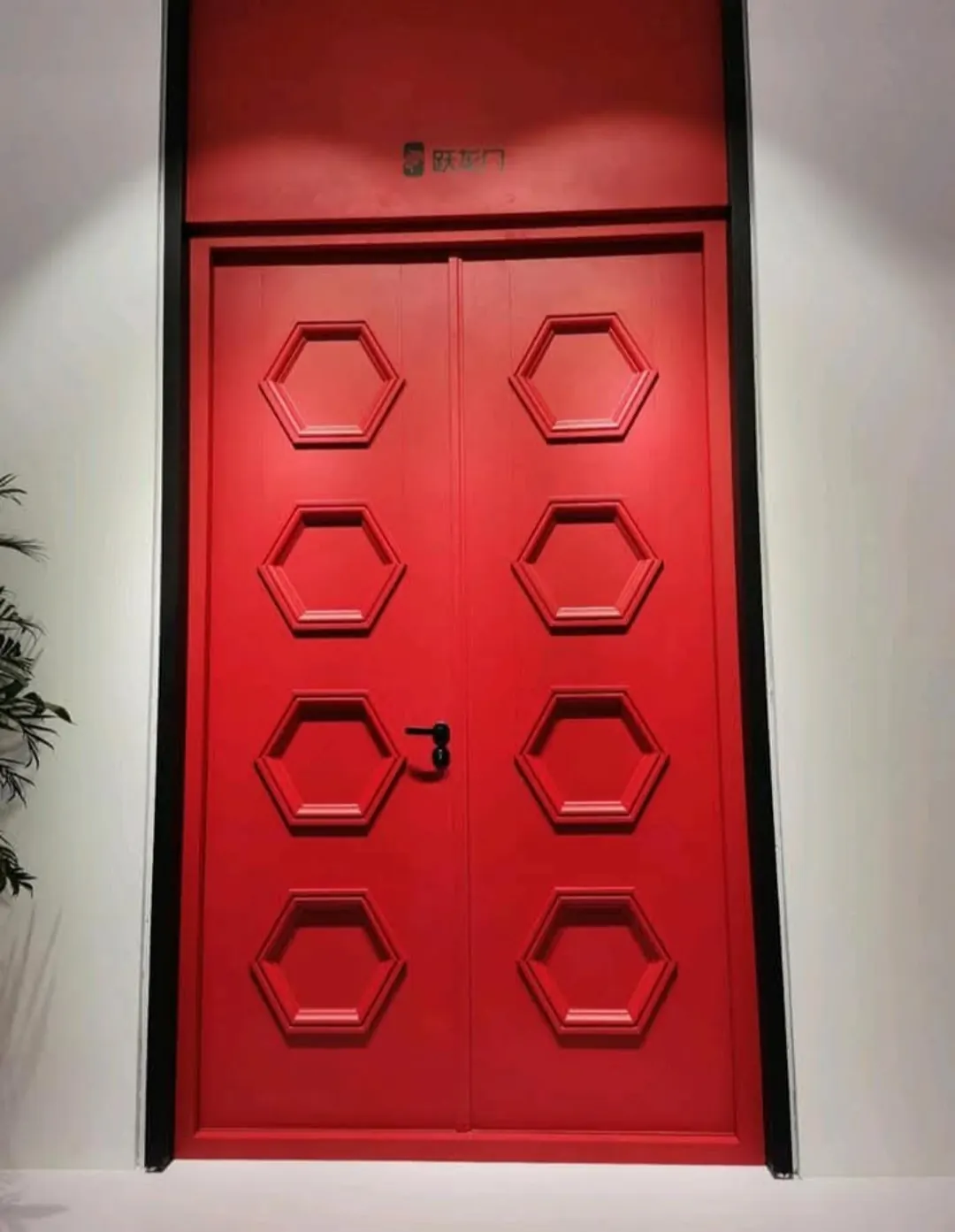 Puerta acorazada de dos hojas lacada en rojo con paneles hexagonales en relieve.